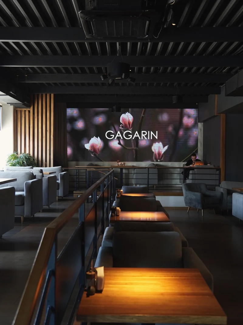 Столы, мягкие кресла и большой экран в основном зале GAGARIN GASTRO BAR