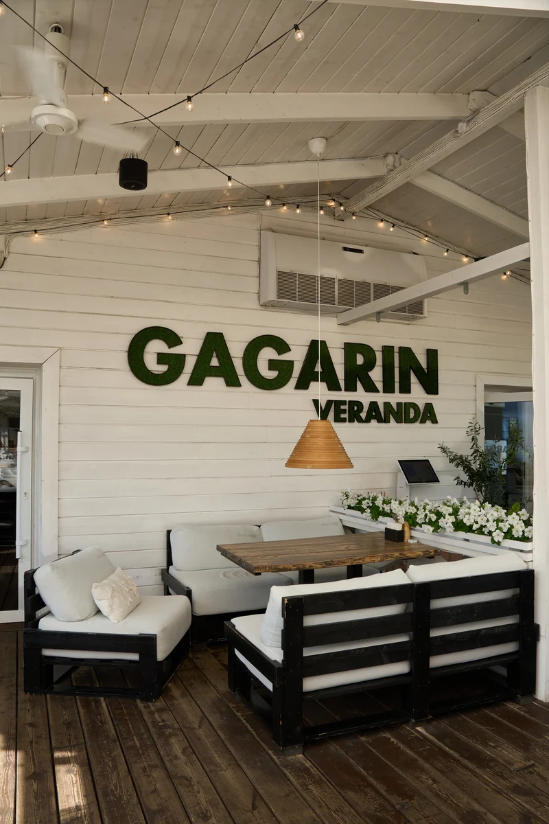 Светлые диваны, деревянный стол, цветы и вывеска GAGARIN VERANDA