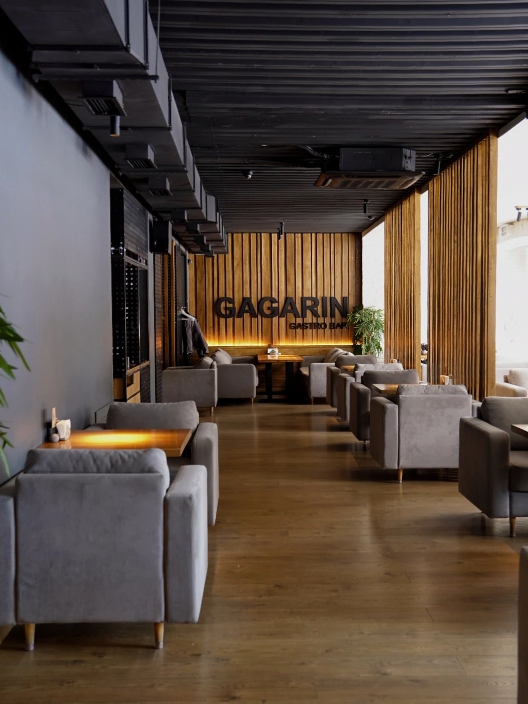 Основной зал GAGARIN GASTRO BAR: серые кресла, деревянные столы и вывеска на стене с тёплой подсветкой